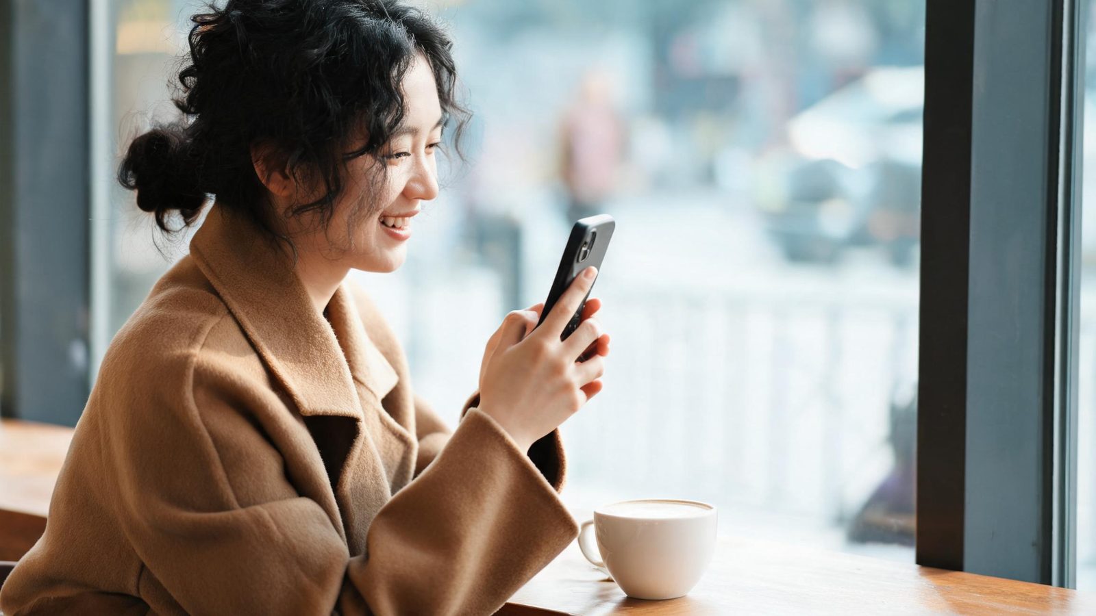 A woman smiles at her phone in a cafe