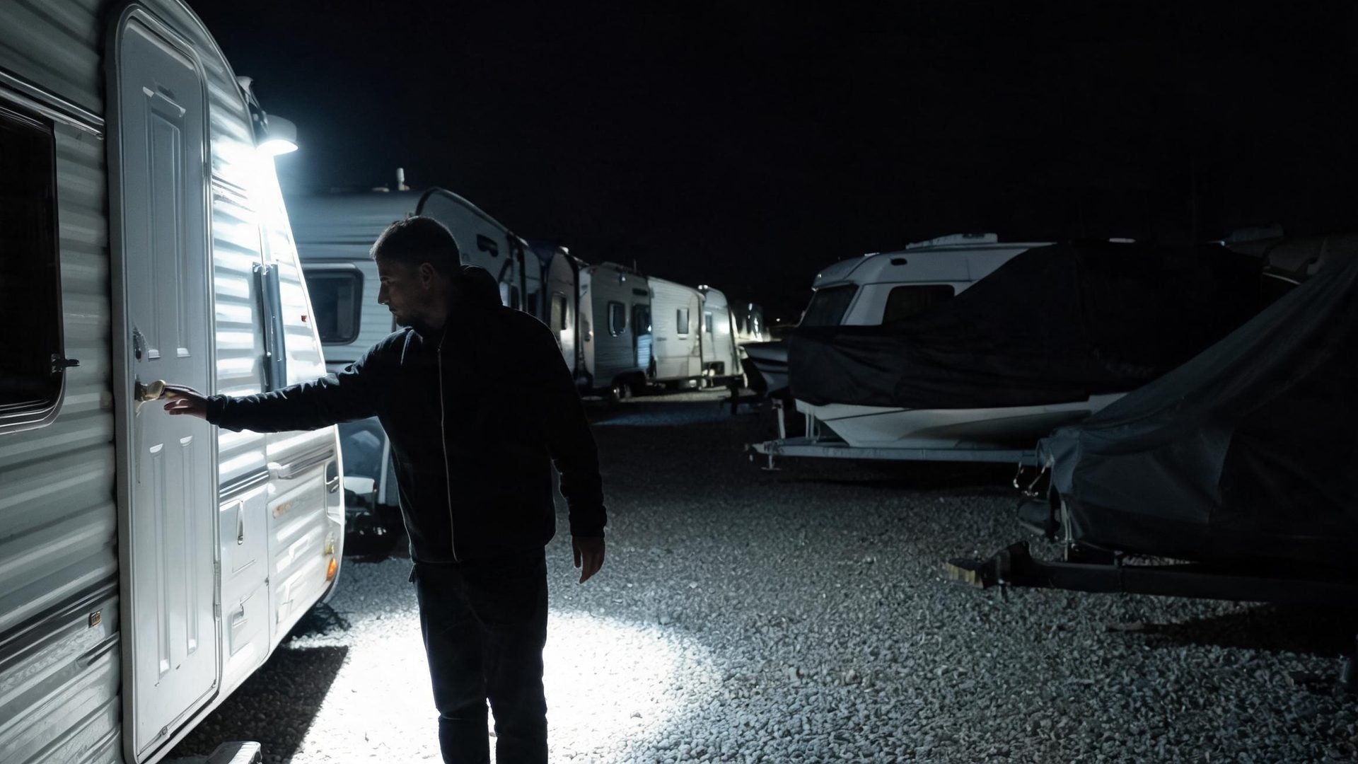 A person trying a trailer door at a storage lot, lit by a spotlight