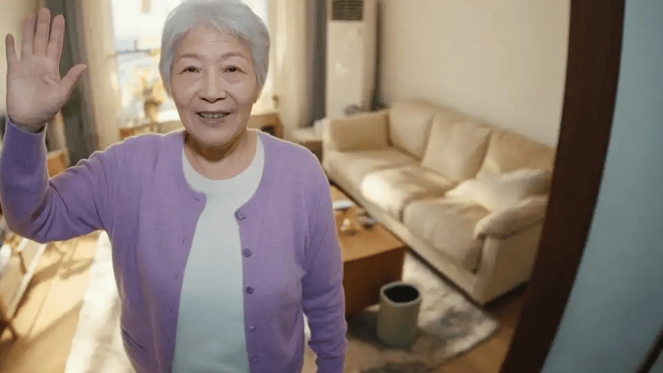 An older woman waves at the camera and talks