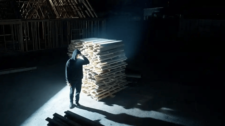 A person by a lumber pile caught in a spotlight at night